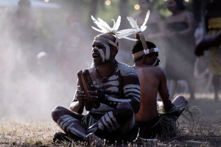 Two Aboriginal men in body paint with white feathers on their heads sitting down