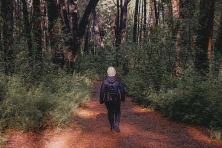 A woman walking along a path towards a thick forest