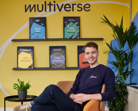 Euan Blair dressed in dark blue sweatshirt and trousers sits in front of a company logo for Multiverse