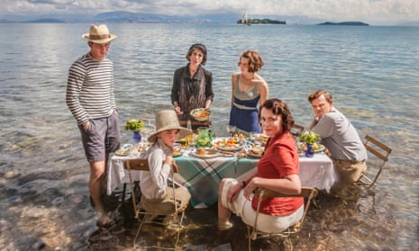 Group cast shot of The Durrells, sitting at a picnic table in shallow water on a beach