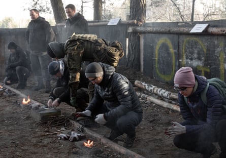People kneel down while learning how to start a fire with twigs