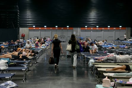 Rows of people resting on camp beds in an exhibition hall