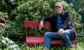 Iain Sinclair sitting on a red bench amid some shrubs