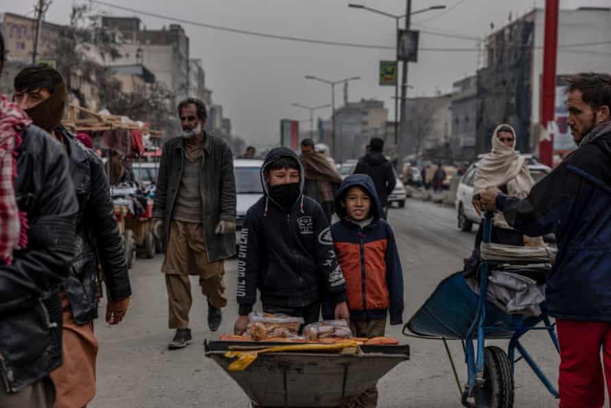 Two boys push a wheelbarrow of biscuits and cake through a market