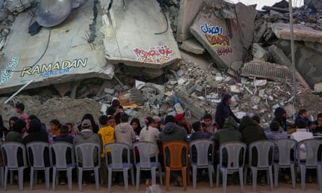 يجلس فلسطينيون على طاولة كبيرة محاطة بأنقاض المباني المدمرة أثناء تجمعهم لتناول وجبة الإفطار في اليوم الأول من شهر رمضان في رفح جنوب قطاع غزة في الأول من مارس/آذار.