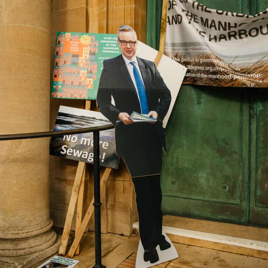 A cardboard cutout of Michael Gove rests against protest signs outside Chichester’s County Hall