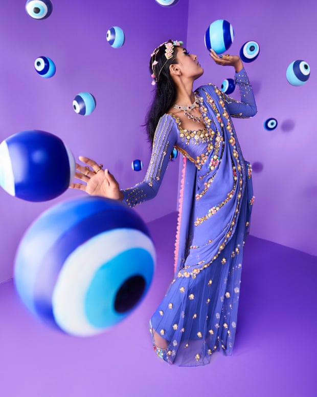A shot of a recent Papa Don’t Preach campaign. A woman is wearing a lavender sari with gold embellishments and is surrounded by beach balls with the evil eye  printed on them. 