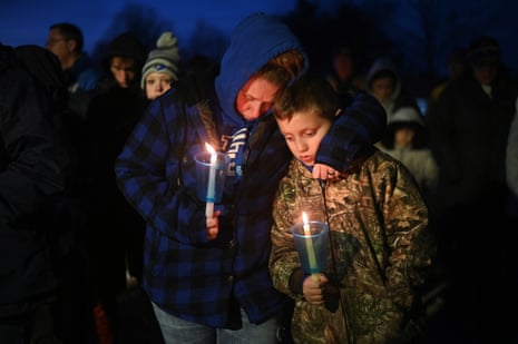 People hug and hold lit candles at a vigil.