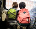 Two boys wearing backpacks sit side by side, looking out of a train window