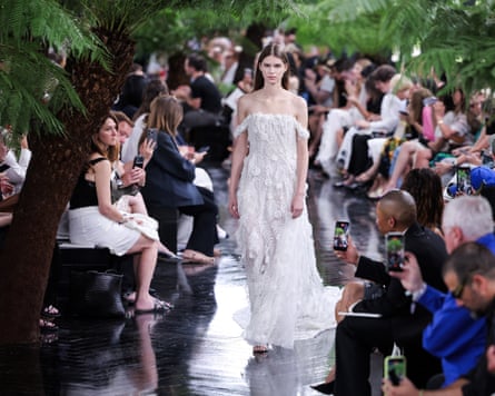 A woman walks down a catwalk wearing a white dropped sleeve dress