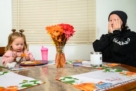 A woman holds her hands to her face as a young child eats chips at a kitchen table