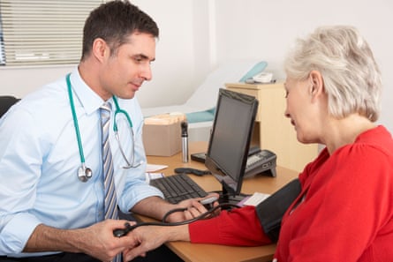 A young male doctor takes a middleaged woman’s blood pressure.