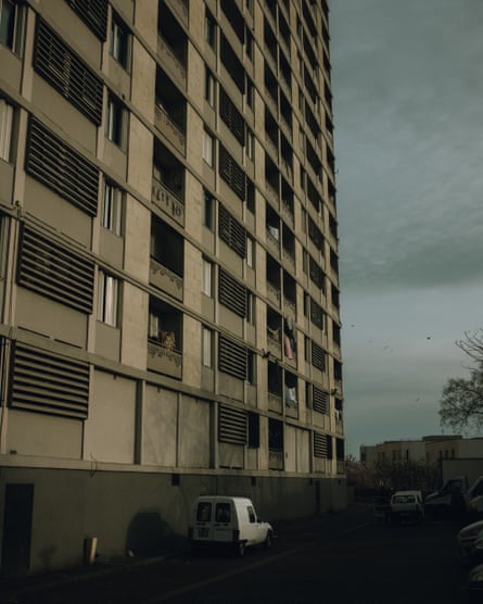 A tall apartment block with rows of balconies and shutters rises beside a street in Marseille
