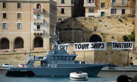A Malta Coast Guards ship patrols as protesters display a banner urging action on migrant rescue.