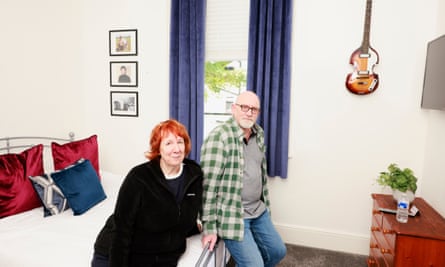 Evelyn and Andy in their room at the Casbah Coffee Club. Evelyn is sitting on the bed and Andy is leaning against it. There are photographs and a guitar on the wall behind them