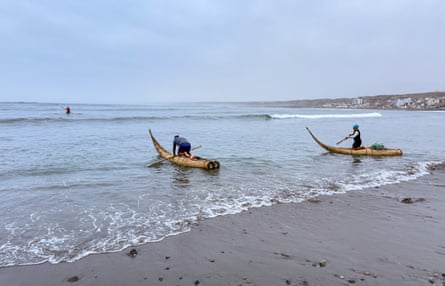 Two people holding paddles push their craft made of reeds into the water.