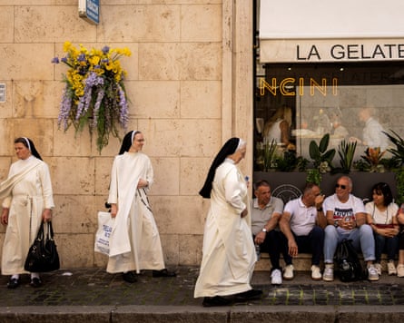 Three nuns in white stand next to a row of tourists sitting in front of a gelat
