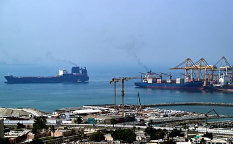 Ships are docked along a pier in the Gulf of Oman