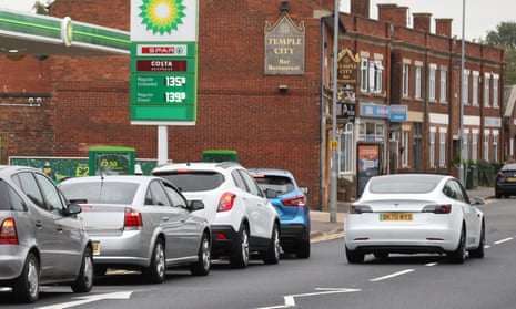 A Tesla electric car drives past cars queueing for fuel at a BP filling station in Peterborough