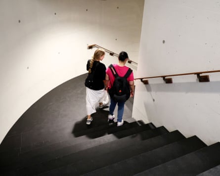 Two women walk down a staircase surrounded by white walls.