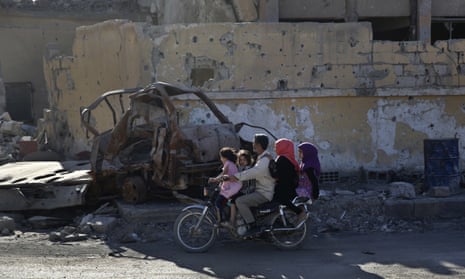 a family rides a motorcycle on a street that was damaged during fighting, Raqqa, Syria.
