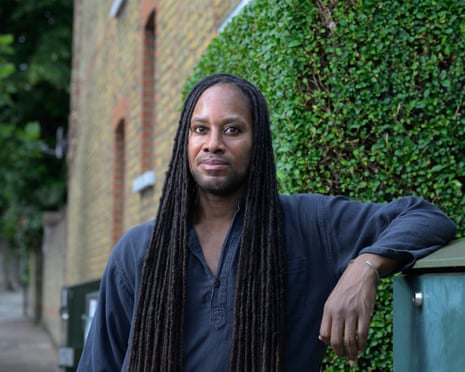 Arday dressed casually poses outside brick building with green vegetation behind him