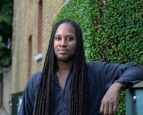 Jason Arday, a Black academic, leans against a wall by greenery