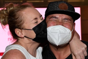 A woman wearing a white singlet and black mask kisses the cheek of a man wearing a cap and white mask at Sydney airport