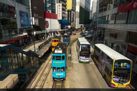 Double-decker trams and buses travel along a busy commercial street lined with retail stores and office buildings
