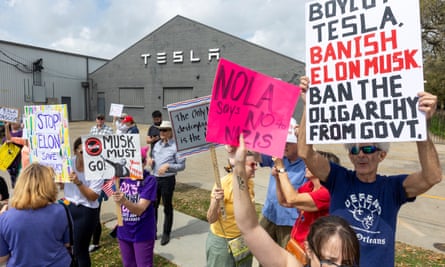 a group of people hold signs with messages like ‘Nola says no to Nazis’ and ‘boycott Tesla, banish Elon Musk, ban the oligarchy from govt’