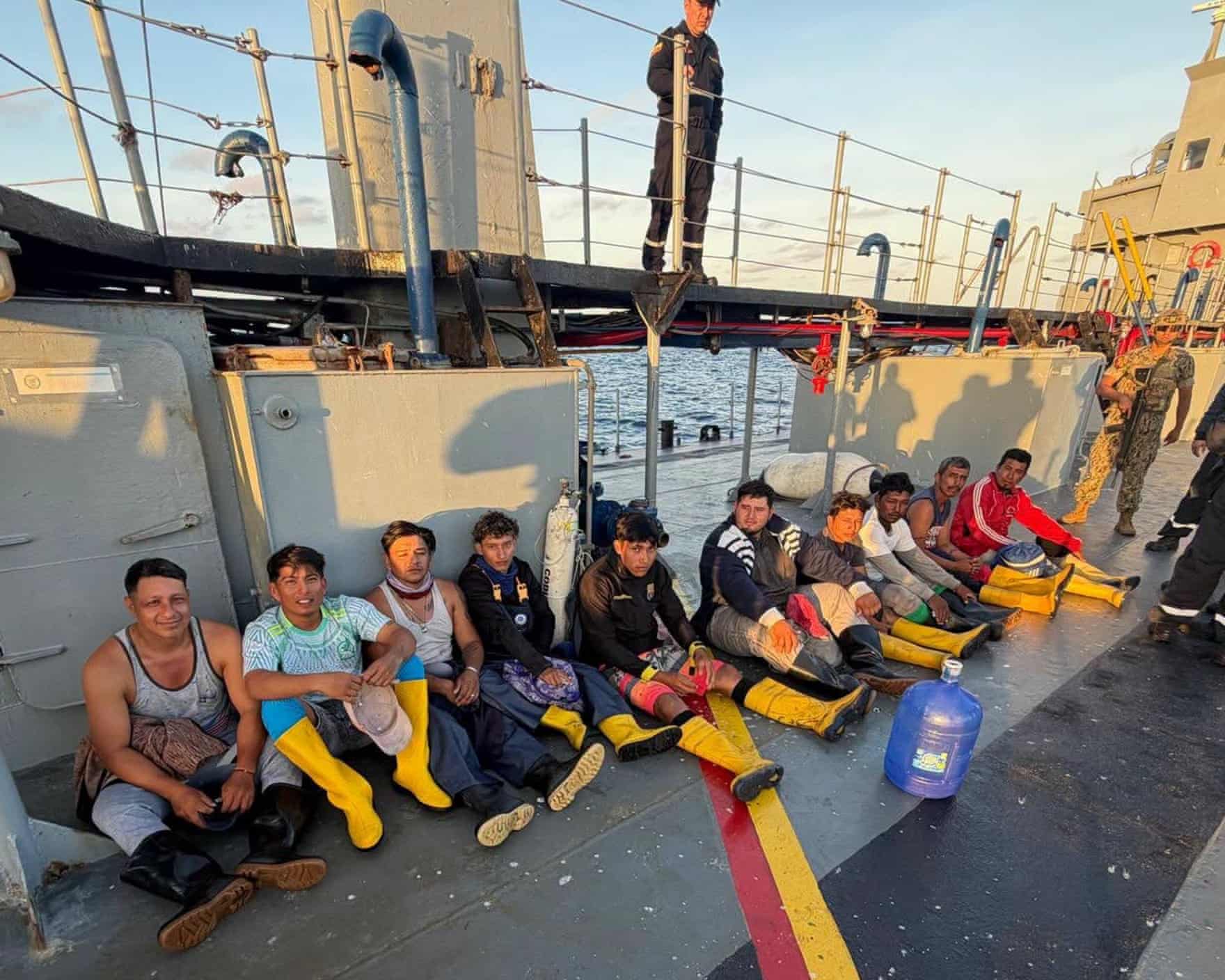 People sitting in a line, many of them wearing yellow rain boots