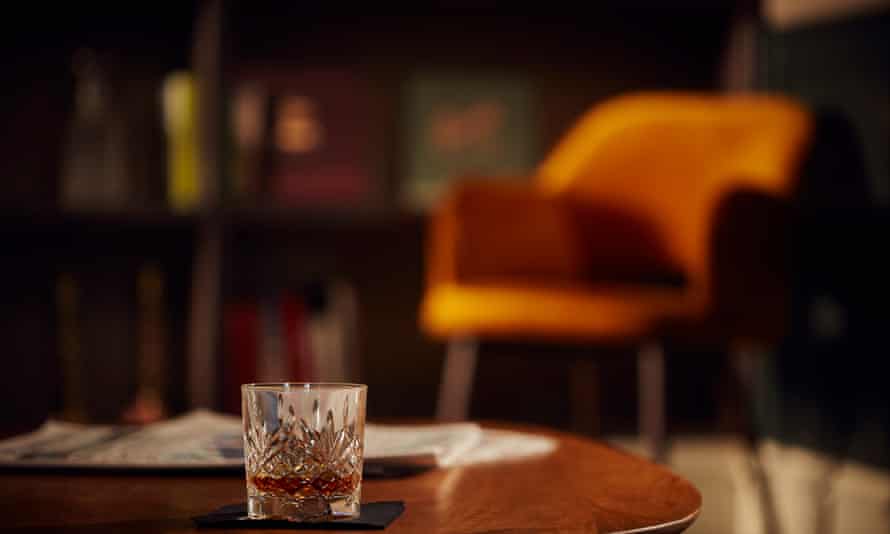 A glass of whisky on a table with an orange chair in the background