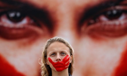 An activist with a red handprint on her face stands in front of a picture of a person with the same red marks on their face as she protests against rape and violence against women on Copacabana beach in Rio de Janeiro in 2016.