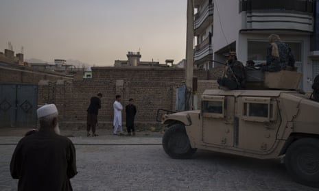 Afghans watch as Taliban fighters ride atop a Humvee