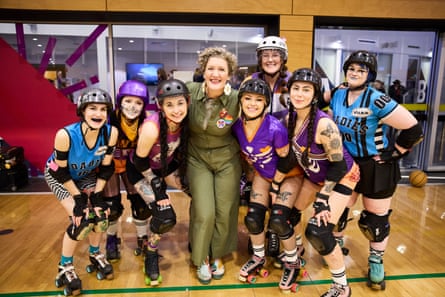 Eight roller derby skaters, many of them women, standing in a close group with Virginia Gay at the centre, all smiling