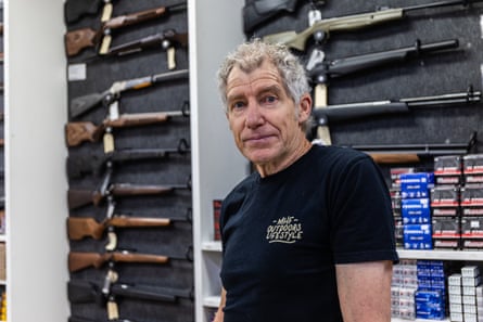 Shane Curley in front of a wall of rifles