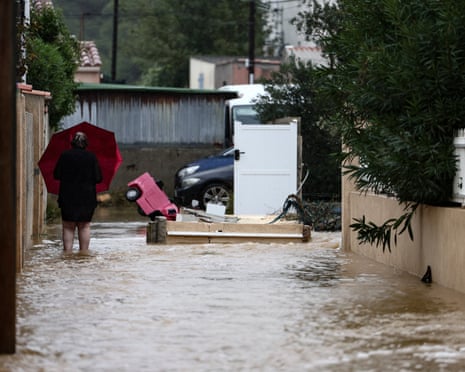 A resident holds a red umbrella while wading through a flooded street