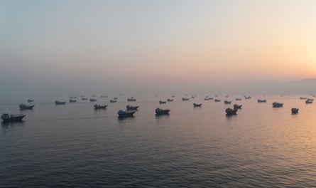 A drone view shows small vessels anchored on a calm sea in the morning light just as the sun is rising.