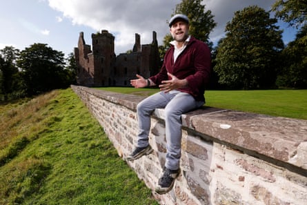Corey Kinnan, wearing a flat cap, jeans and trainers, sits on a stone wall, gesturing, with the ruined Redcastle behind him Corey Kinnan, wearing a flat cap, jeans and trainers, sits on a stone wall, gesturing, with the ruined Redcastle behind him