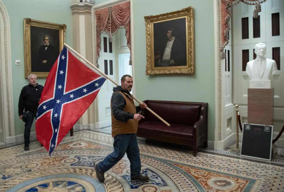 A supporter of Donald Trump carries a Confederate flag inside the US Capitol – next to portraits of John C Calhoun, left, and Charles Sumner, pro- and anti-slavery politicians of the mid-19th century.