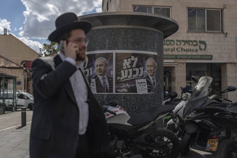 A Jewish man on the phone walks past a poster of Benjamin Netanyahu.