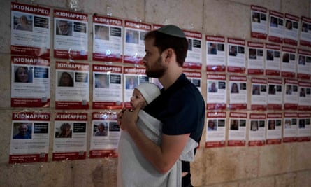 A man holds his baby as he looks at posters of hostages being held in Gaza