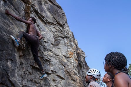 Three people look up at a man climbing on a rockface