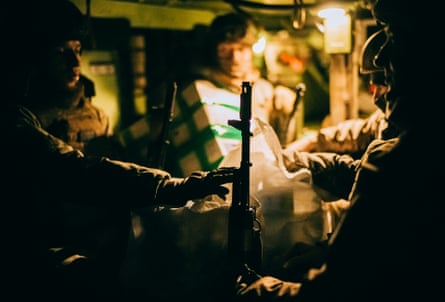 Drone pilots sit in the glow of a light inside the vehicle, cramped together and holding weapons
