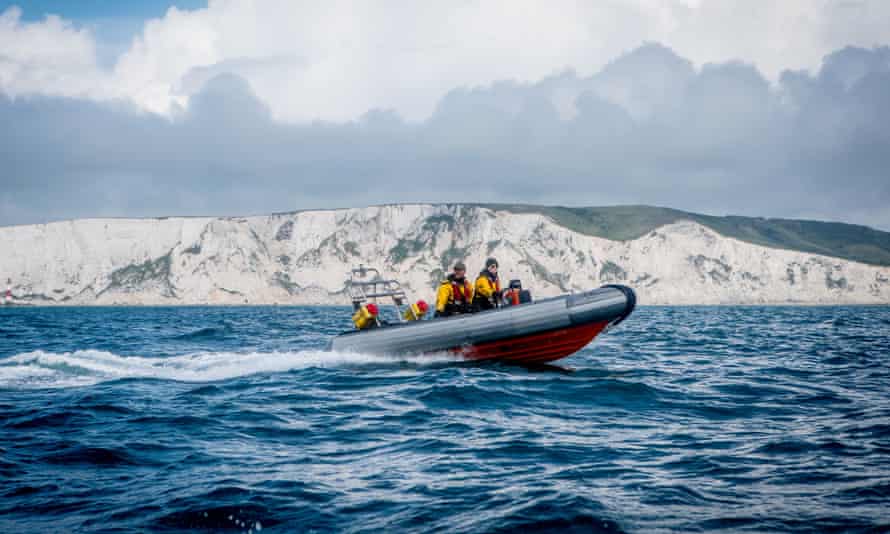 A small boat in the strait passes the white cliffs of the south coast