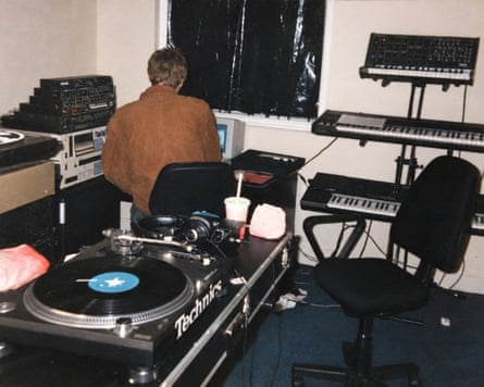 A man works at a mixing desk beside a turntable and keyboards in a home studio