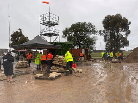 People in yellow and orange hi-vis prepare sandbags in a muddy area