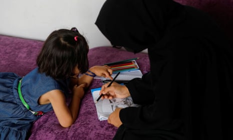 A woman in a black chador draws on a piece of paper watched by a young girl, with the angle of photo meaning both faces are obscured by hair and hijab, presumably to protect their identity
