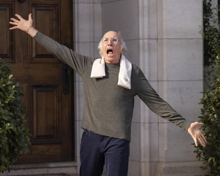 Larry David shouts with arms outstretched, wearing an ice pack scarf around his neck