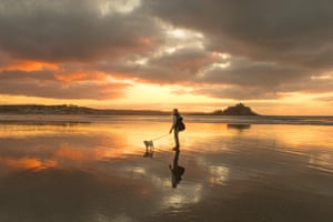 A Cornish dog walker at sunrise on the beach at St Michaels Mount, Marazion